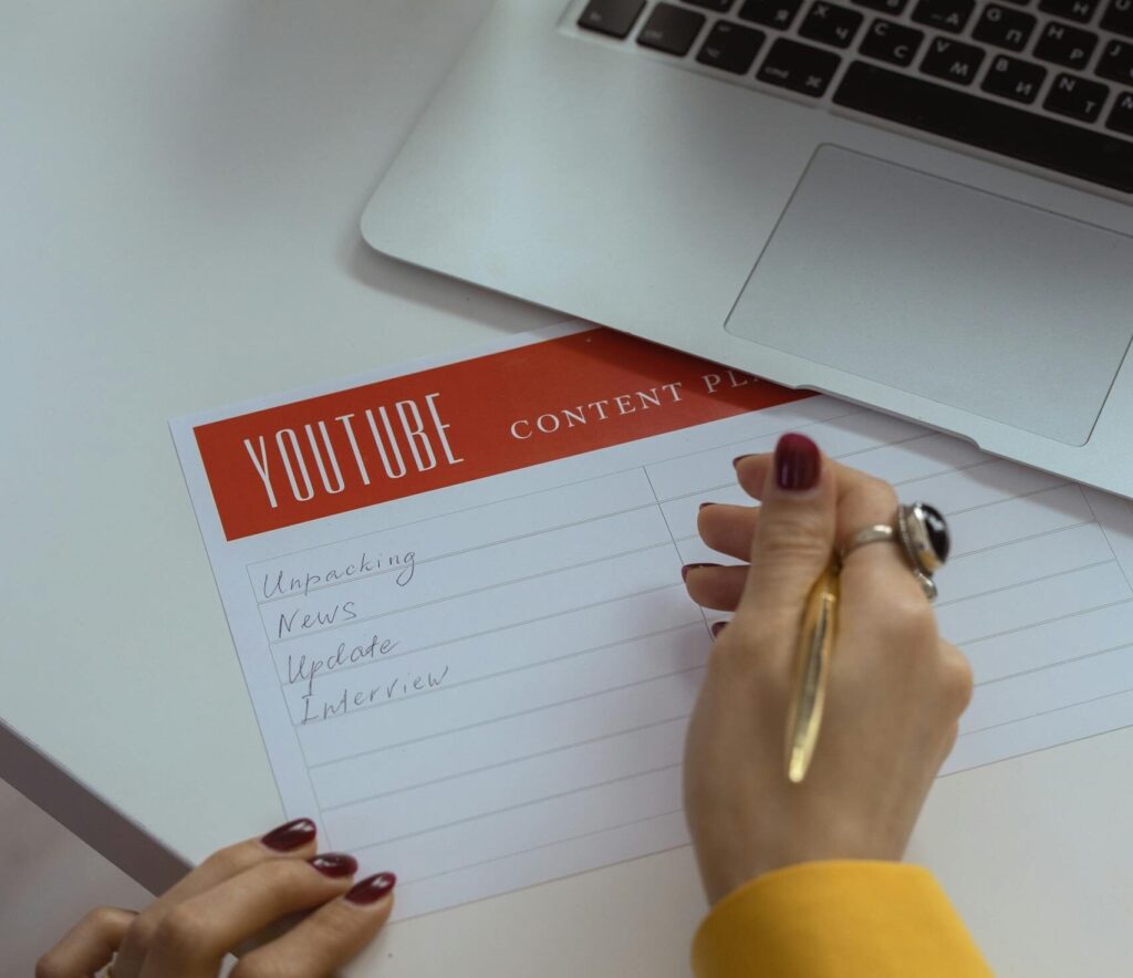 Woman with manicured nails writes YouTube content ideas in office setting.